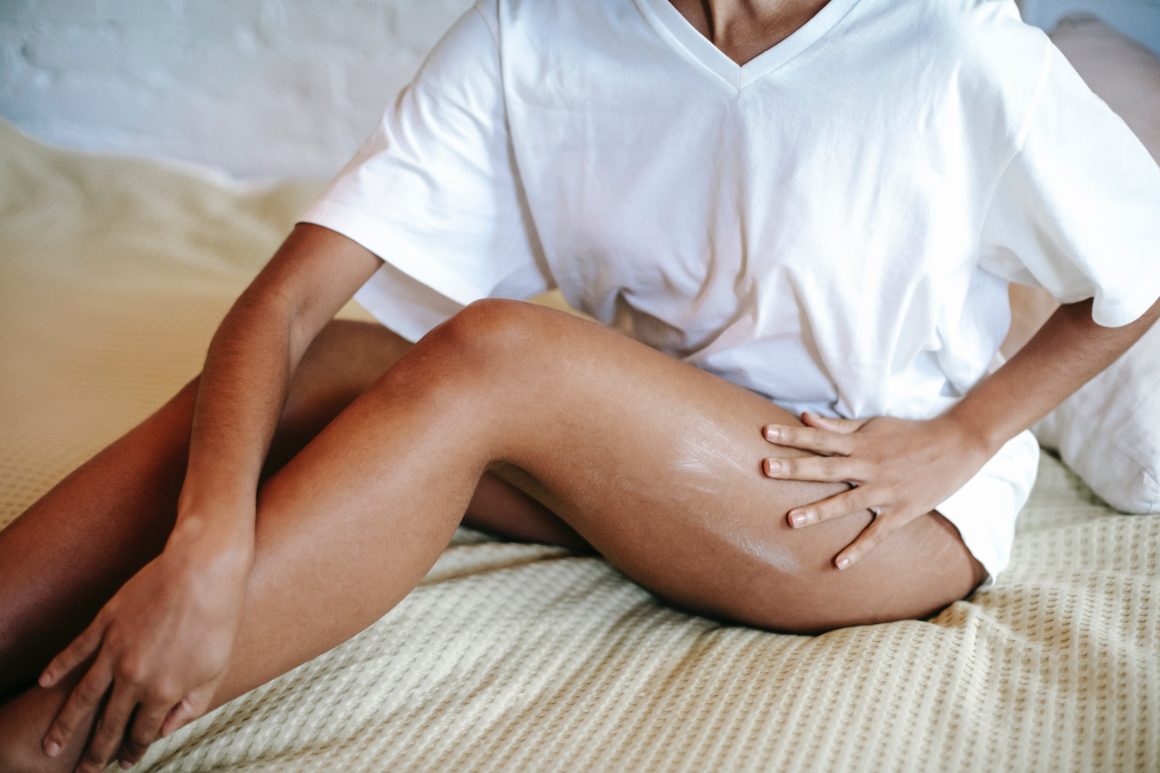 Woman sitting on a bed applying lotion to her legs